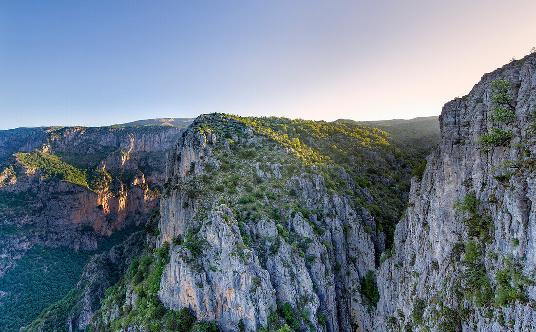 Lichtstrahlen der frühen Morgensonne treffen auf die Klippen und Bäume am Rande der Vikos-Schlucht am Aussichtspunkt Beloi bei Vradeto; Epirus Griechenland