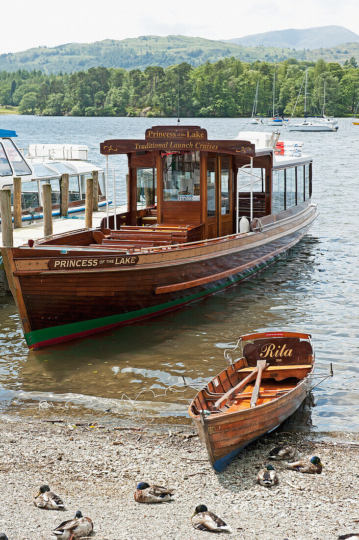 Ein großes und ein kleines Holzboot nebeneinander im seichten Wasser entlang des Strandes; England