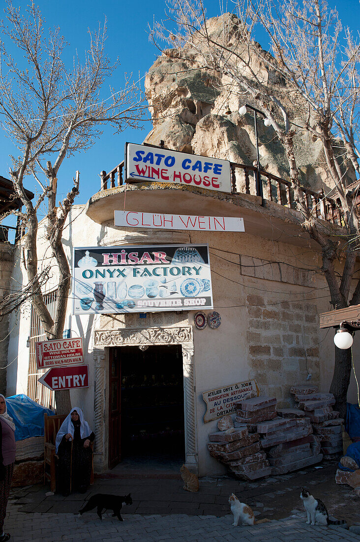 Ein Gebäude mit zahlreichen Schildern an der Ecke und Katzen, die davor sitzen; Ortahisar Nevsehir Türkei