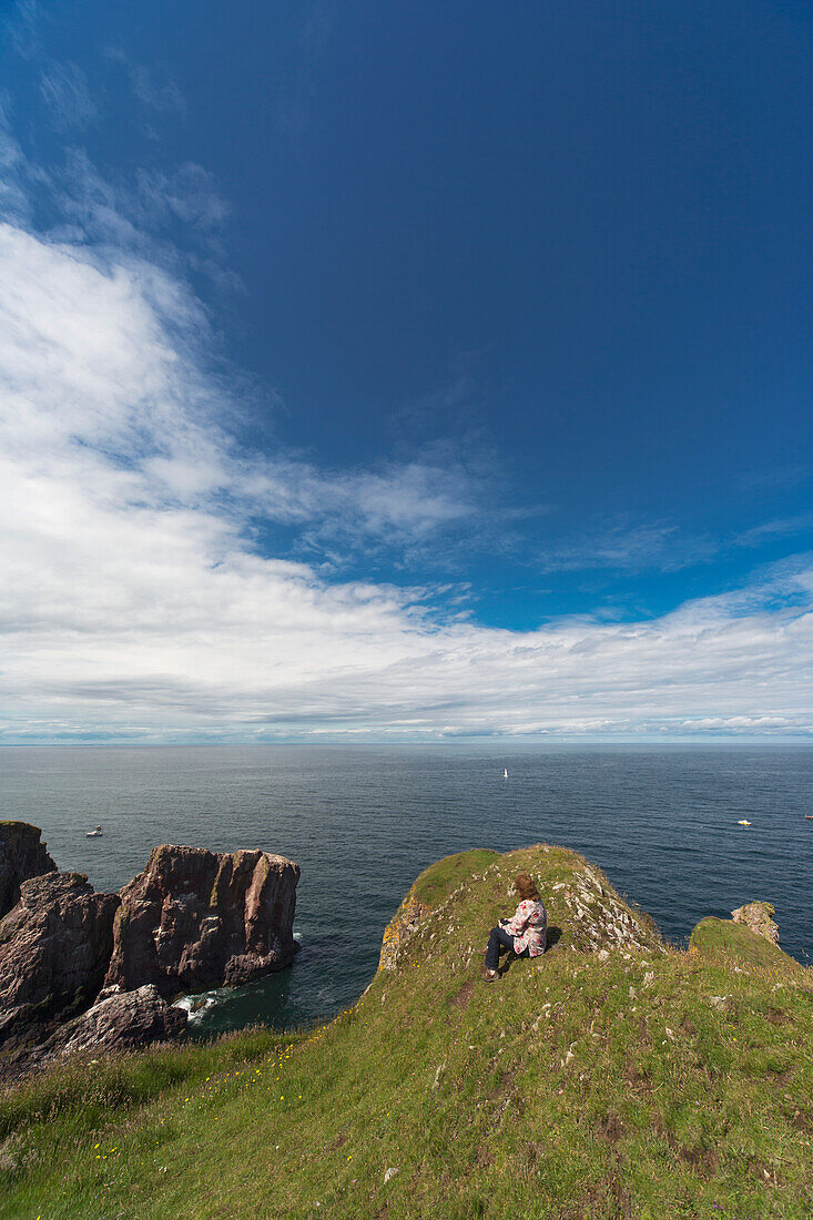 Eine Frau sitzt auf dem Gras entlang der Küste; St Abbs Head Scottish Borders Schottland