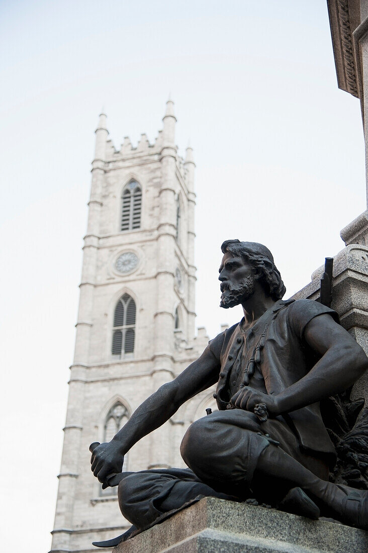 A Statue Of A Male Figure With A Clock Tower In The Background; Montreal Quebec Canada