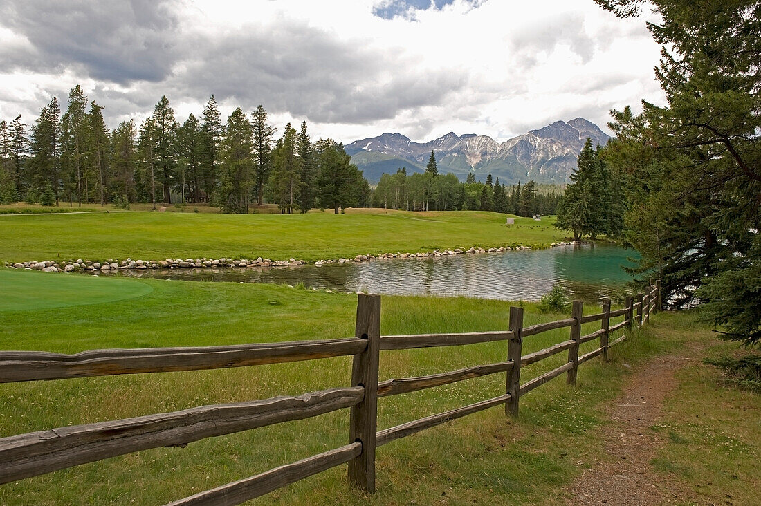 Green Grass Field Lake With The Mountains In The Distance; Alberta Canada