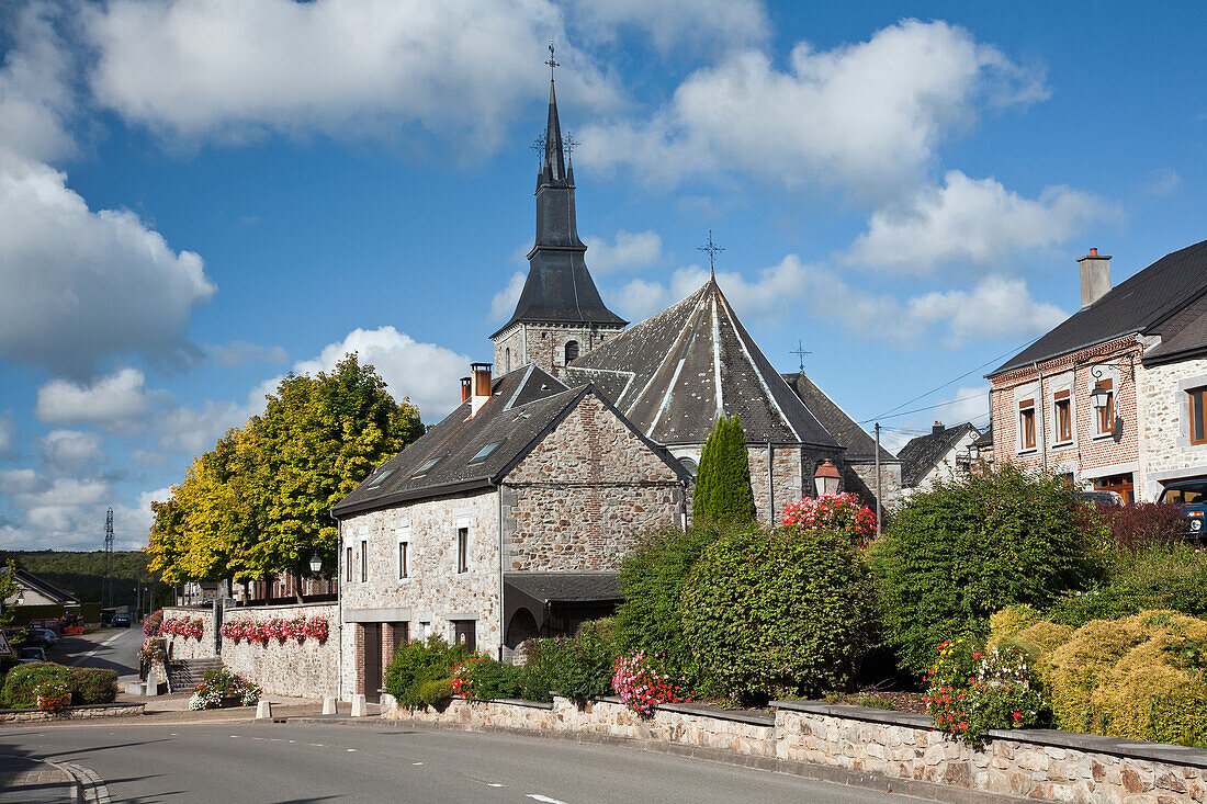 Eine Kirche und hängende Blumenkörbe an einer Steinmauer entlang einer Straße; Hergnies Ardennes Frankreich