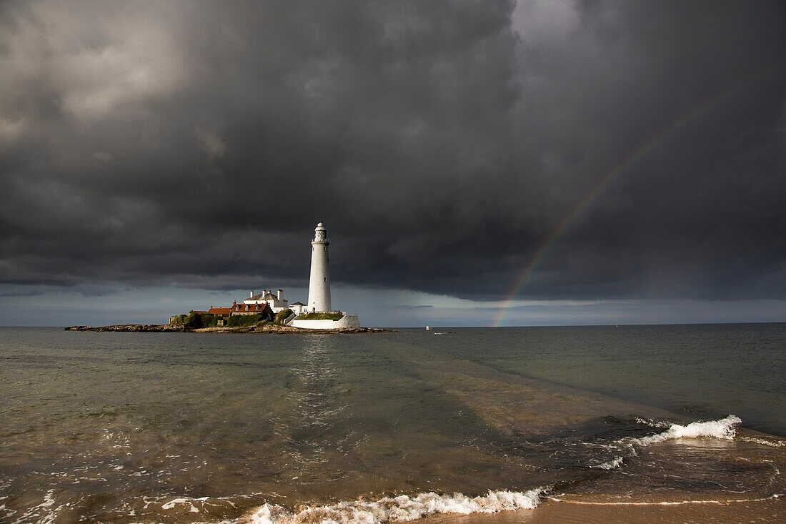 Weißer Leuchtturm, beleuchtet vom Sonnenlicht unter einem dunklen, stürmischen Himmel mit einem Regenbogen; St. Mary's Island Northumberland England