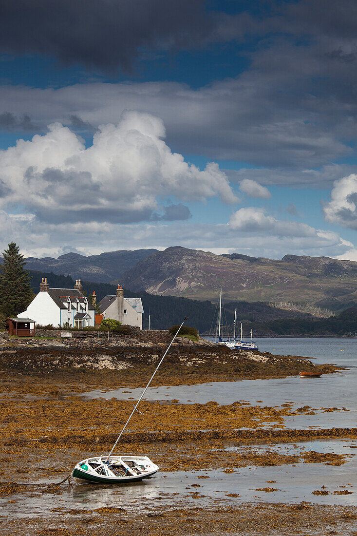 A Boat Lays In The Shore At Low Tide With Houses Along The Coastline; Plockton Highlands Scotland