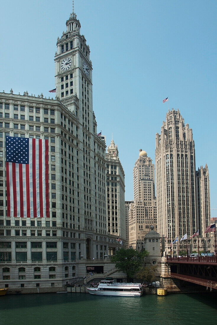 American Flag Hanging On The Side Of A Building With A Clock Tower Along The Chicago River; Chicago Illinois United States Of America