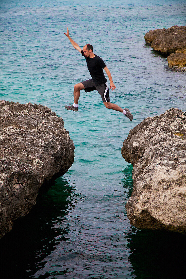 Aruba, Orangestad, Mann springt über Felsen im tropischen Meer