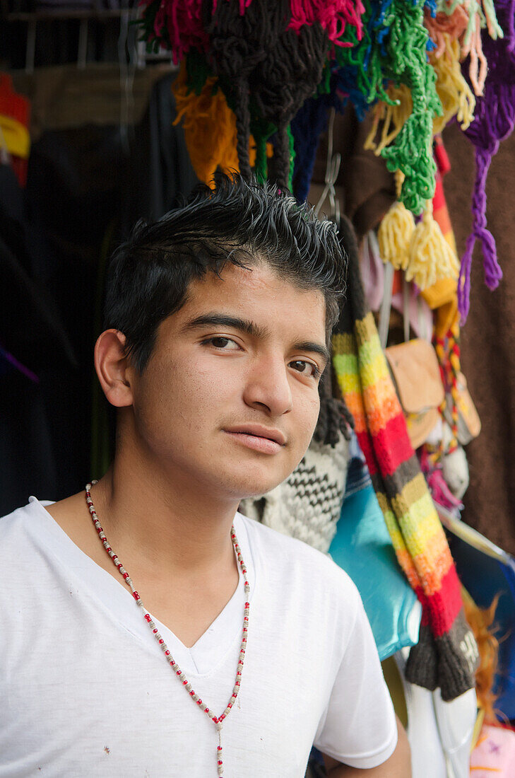 Portrait of boy standing in front of colorful scarves and hats; Guanajuato, Guanajuato State, Mexico