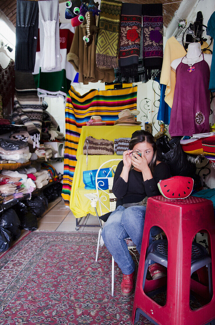 Souvenir vendor applying makeup in her shop; Guanajuato, Guanajuato State, Mexico