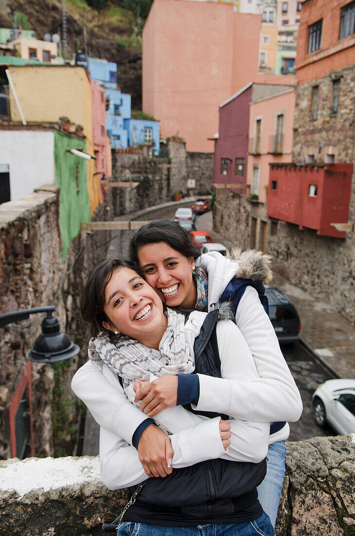 Mexico, Guanajuato State, Guanajuato, Two young women hugging and laughing in downtown area