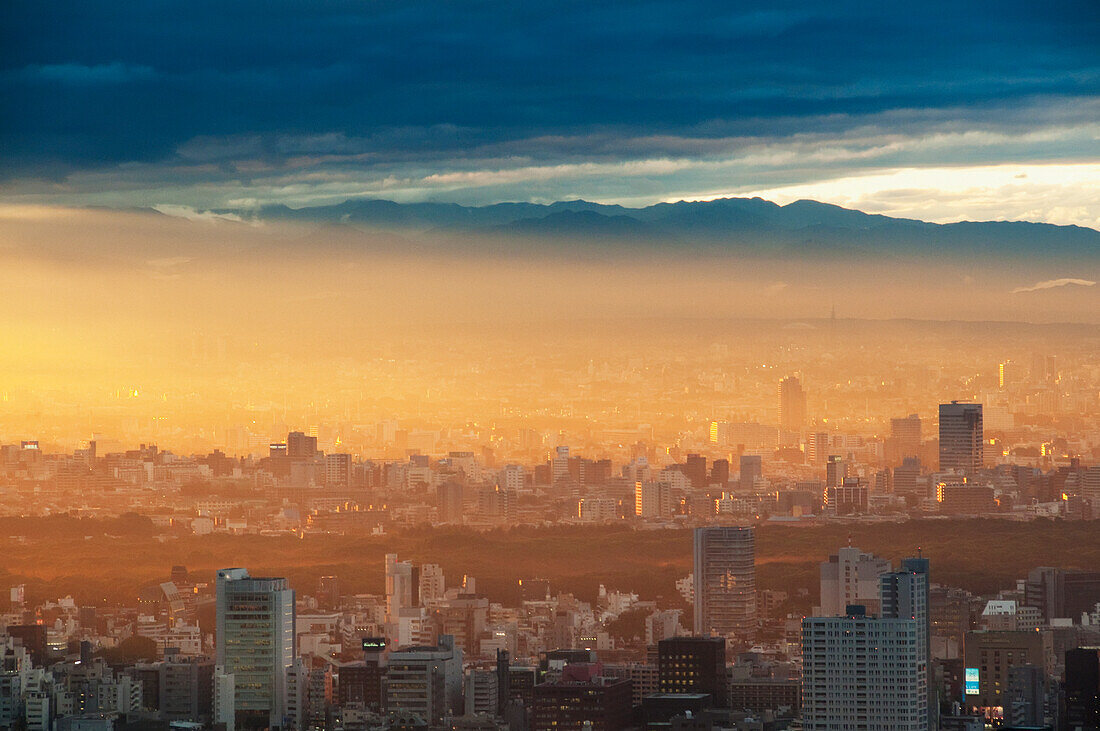 Japan, Tokio, Sonnenlicht bei Sonnenaufgang über einer Stadtlandschaft mit Bergen im Hintergrund