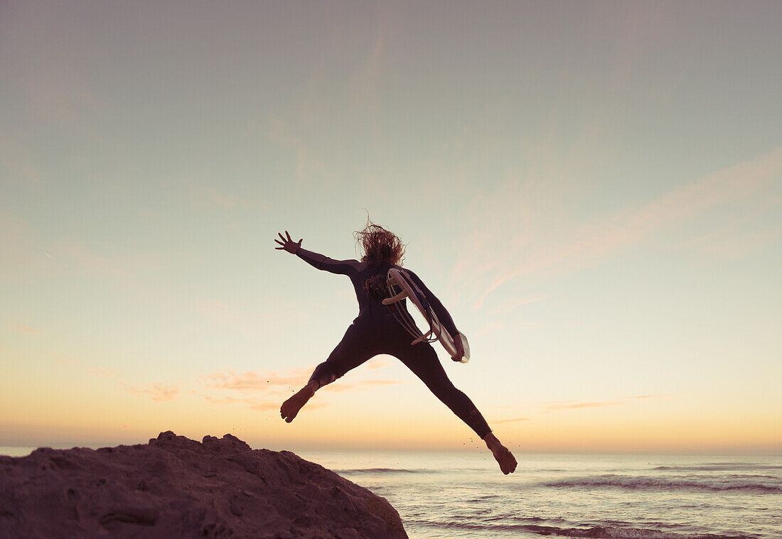 Spain, Andalusia, Cadiz, Costa de la Luz, Surfer jumping from rock; Tarifa