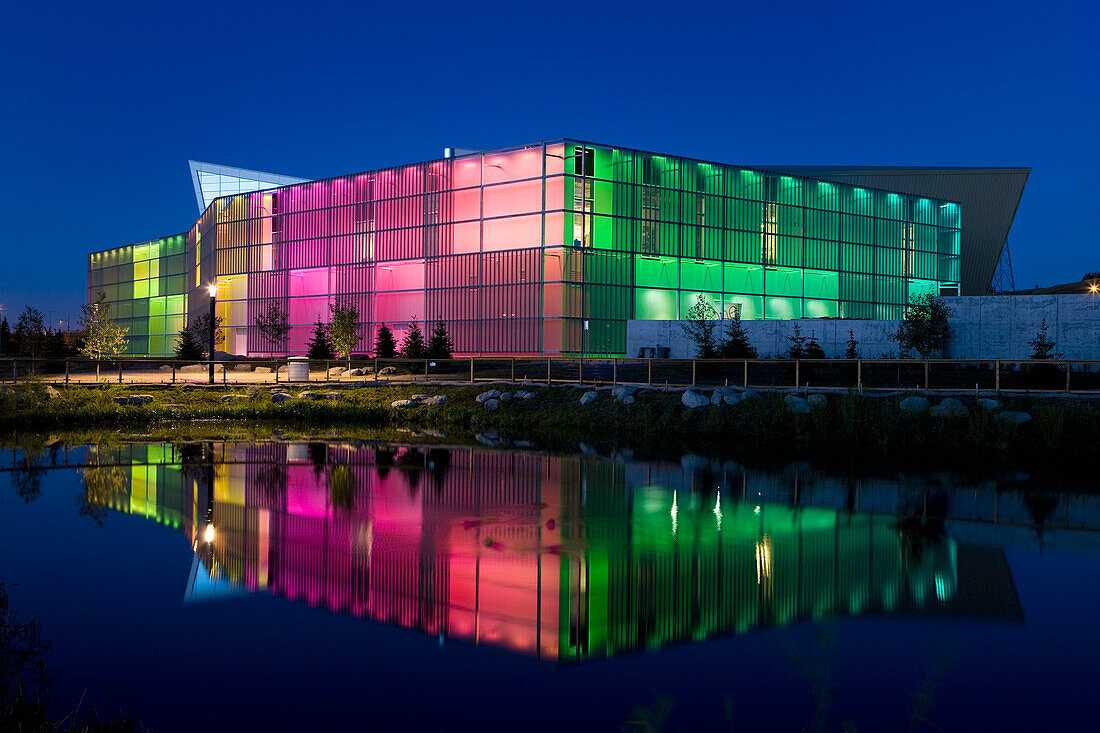 Night Shot Of Building Lit By Colourful Lights And Reflecting In Pond; Calgary, Alberta, Canada