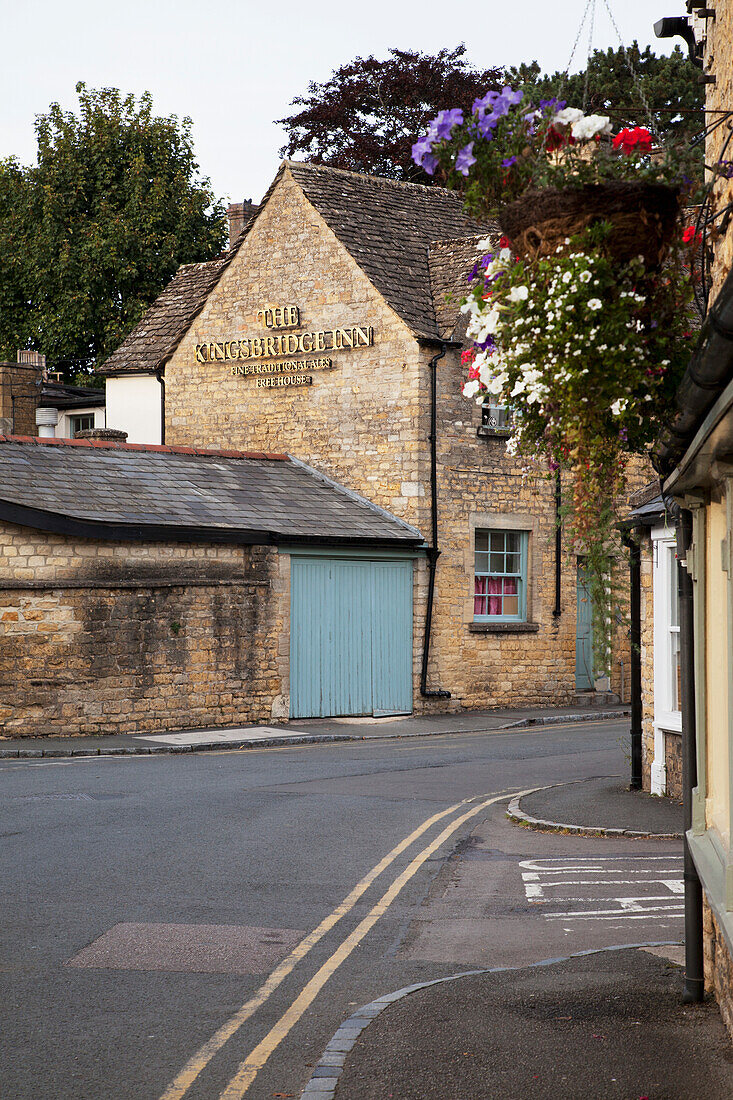 A Street With Flower Baskets Hanging From The Side Of A Building And The Kingsbridge Inn; England