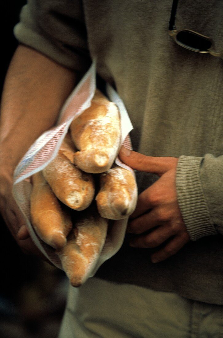 Mann trägt Baguettes (in Papier eingeschlagen) unterm Arm