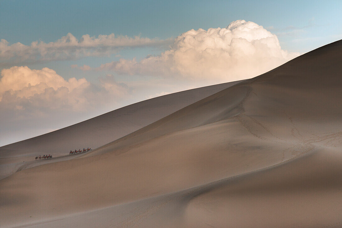 Tourists And Camels Climbing The Slopes Of Singing Sand Mountain; Jiuquan, Gansu, China