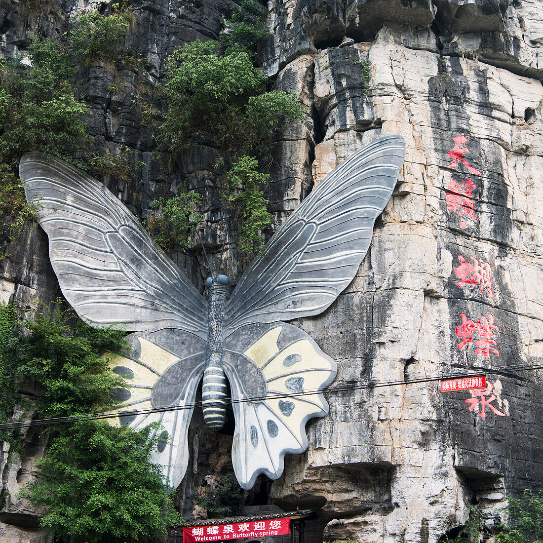 A Large Butterfly Mounted On A Mountainside Above A Sign; Guilin, Guangxi, China