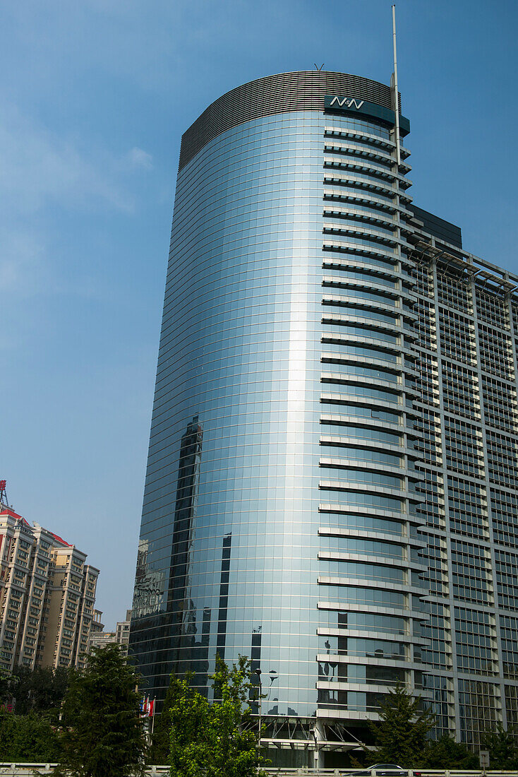 Ein Wolkenkratzer mit einer abgerundeten Seite, in der sich andere Gebäude in der Glaswand spiegeln; Peking, China
