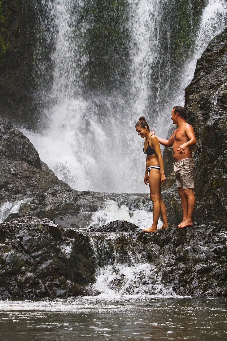 A Couple Stands By The Gorgeous Piroa Falls By The Waipu Gorge; Waipu, New Zealand