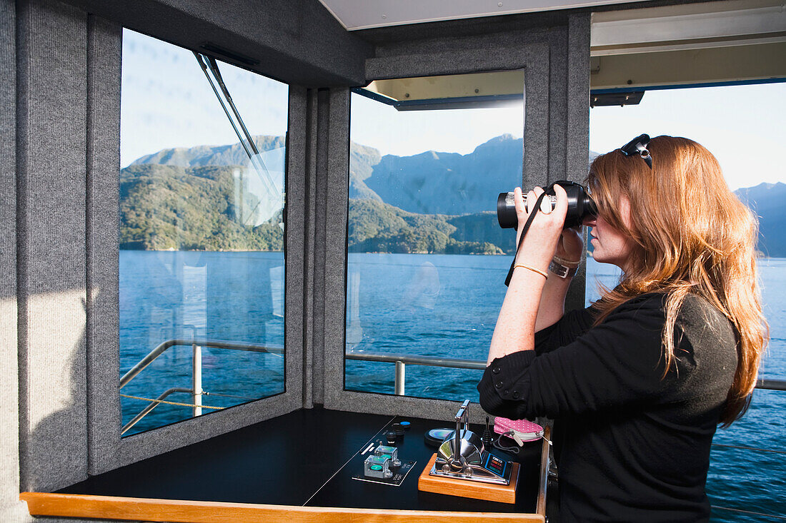 Eine Frau betrachtet die Fjorde durch ein Fernglas auf der Fahrt zum Doubtful Sound; Neuseeland