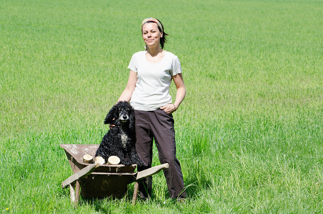A Woman Standing In A Grass Field With Her Dog In A Wheelbarrow; Locarno, Ticino, Switzerland