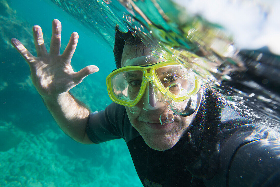 Ein männlicher Taucher winkt Hallo unter Wasser; Utila Island, Honduras