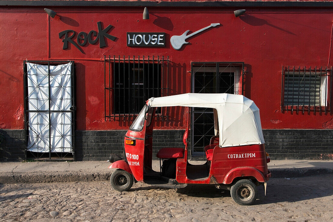 A Red Building With A Sign For Rock House And A Red Motor Cab Sitting Outside; Copan, Honduras
