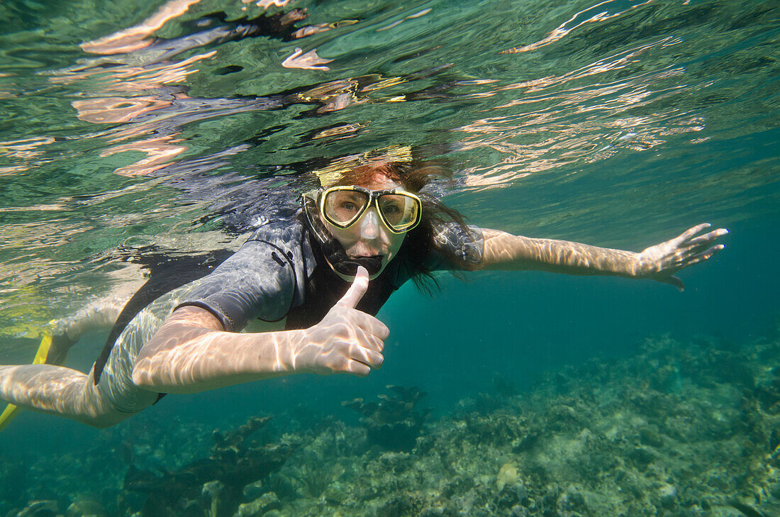 Eine Frau beim Schnorcheln und Daumen hoch unter Wasser; Utila Island, Honduras