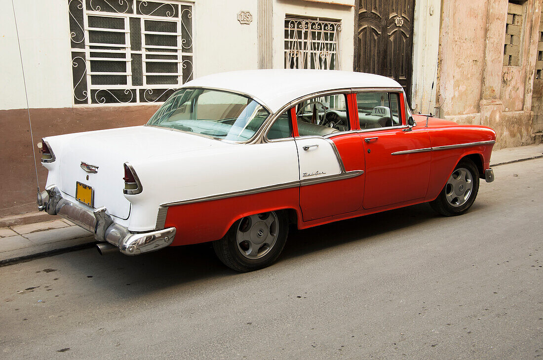 Rotes und weißes Chevy Belair Taxi vor einem Stuckgebäude; Havanna, Artemisa, Kuba