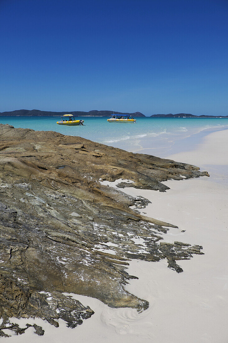 Felsformationen und weißer Sand am Whitehaven Beach mit ankernden Booten entlang der Whitsunday Islands in Queensland, Australien