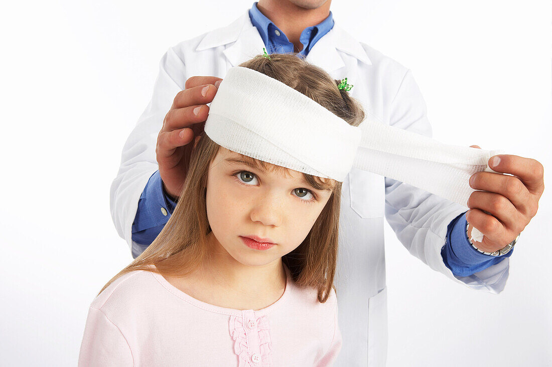 Arzt wickelt Verband um den Kopf eines Mädchens