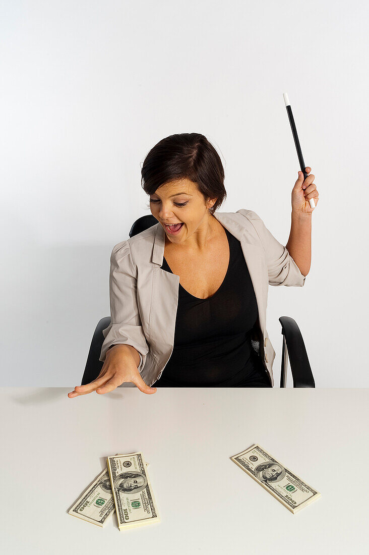 Mittelerwachsene Frau zaubert mit Zauberstab und 100-Dollar-Scheinen