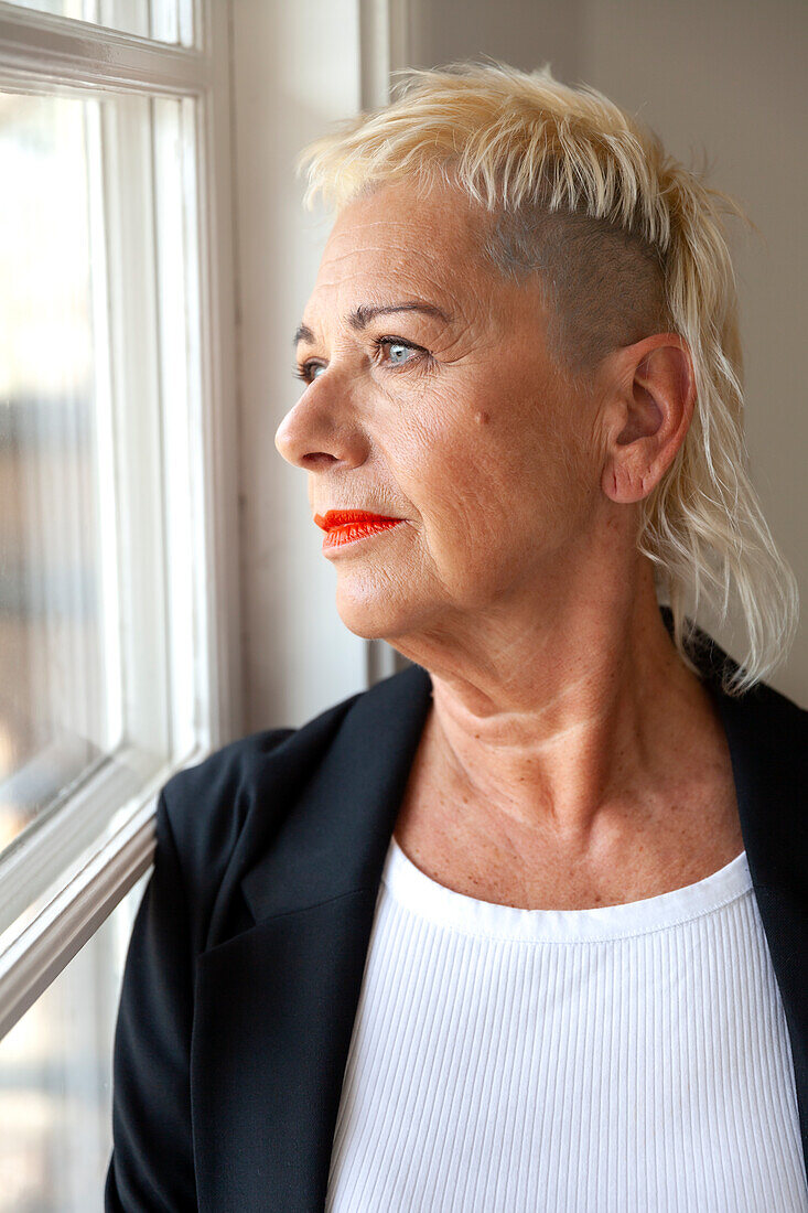 Porträt einer modischen Seniorin, die durch ein Fenster schaut