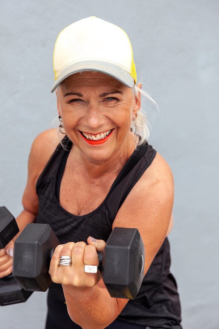 Portrait of fit senior woman with cool haircut holding dumbbells
