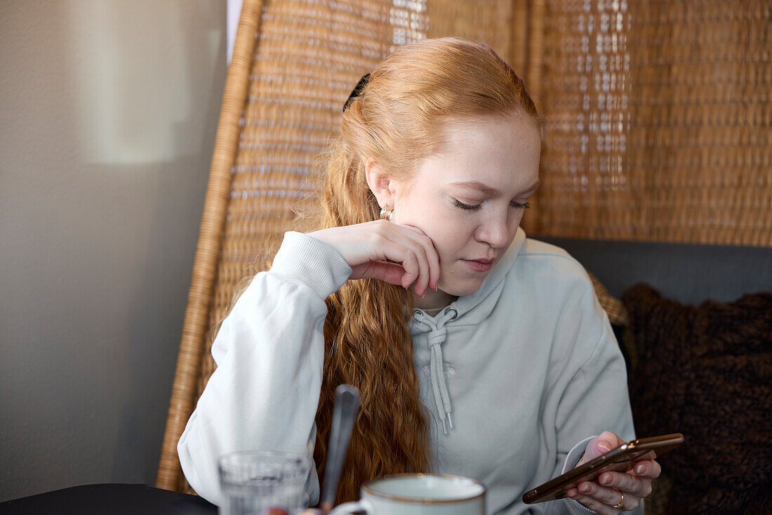 Young woman using phone and checking social media in cafe