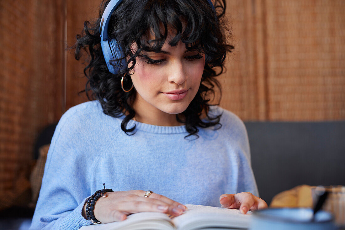 Junge Frau mit Kopfhörern, die beim Lernen ein Buch liest