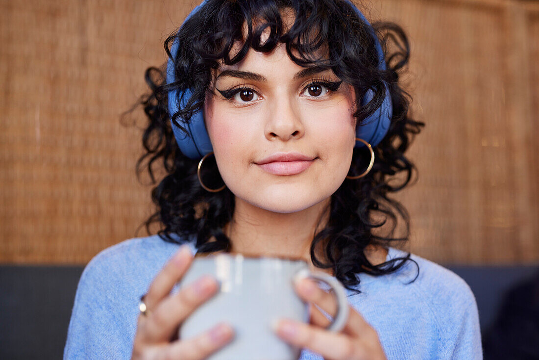 Portrait einer jungen Frau mit Eyeliner-Make-up und Kopfhörern beim Kaffeetrinken
