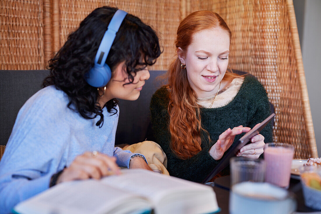Young women, one with red hair and one with dark curly hair, using digital tablet