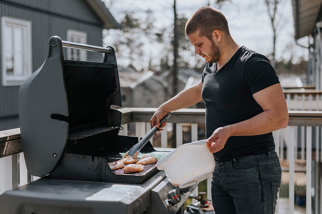 Mann auf Balkon beim Hähnchen grillen