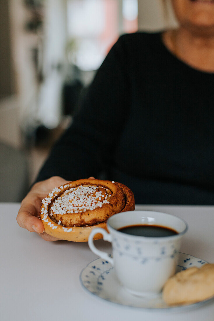 Hand holding cinnamon bun, coffee on foreground