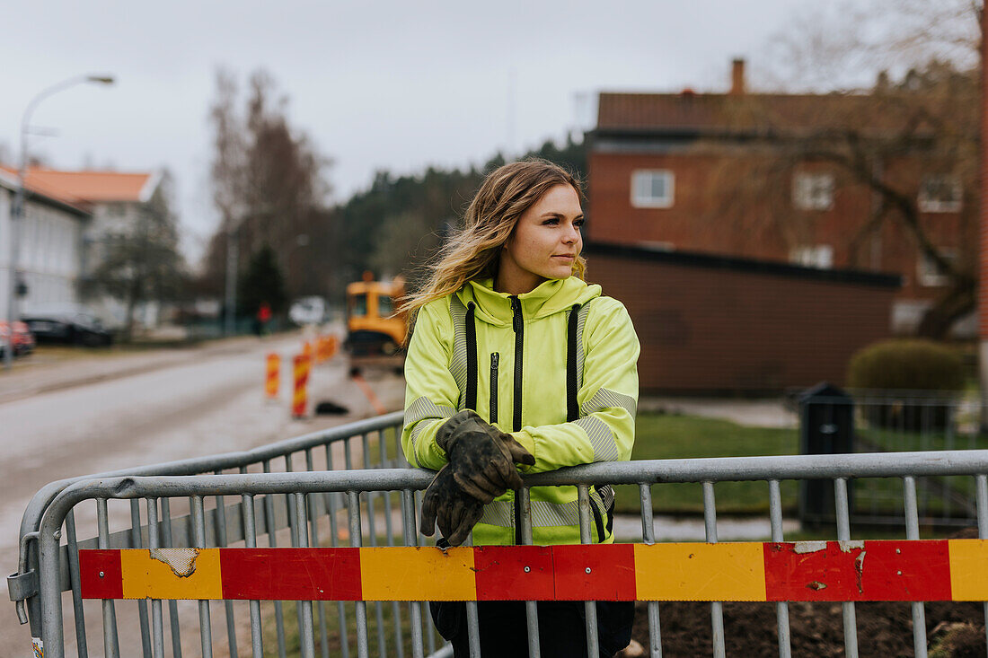 Straßenbauarbeiterin lehnt sich an Verkehrsschranke