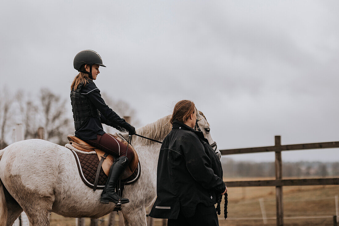 Mädchen reitet mit Reitlehrerin, die neben ihr hergeht