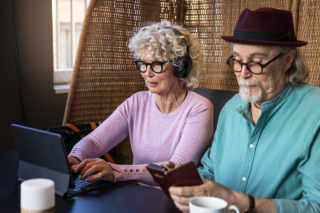 Senior couple sitting in cafe looking at cell phone and digital tablet