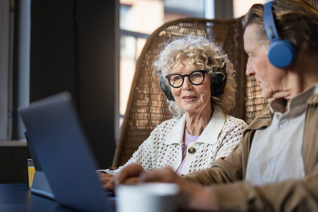 Senior couple sitting in cafe working on digital tablet and laptop