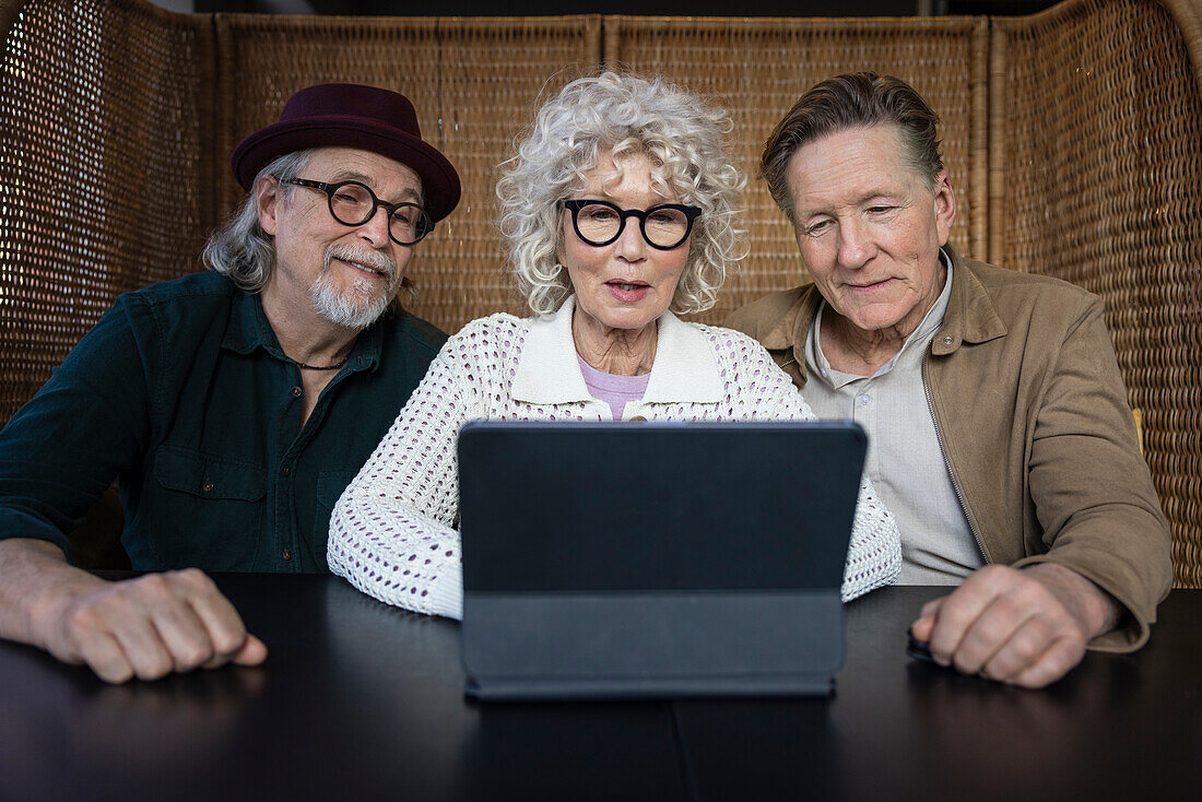 Senior friends sitting in cafe looking at digital tablet