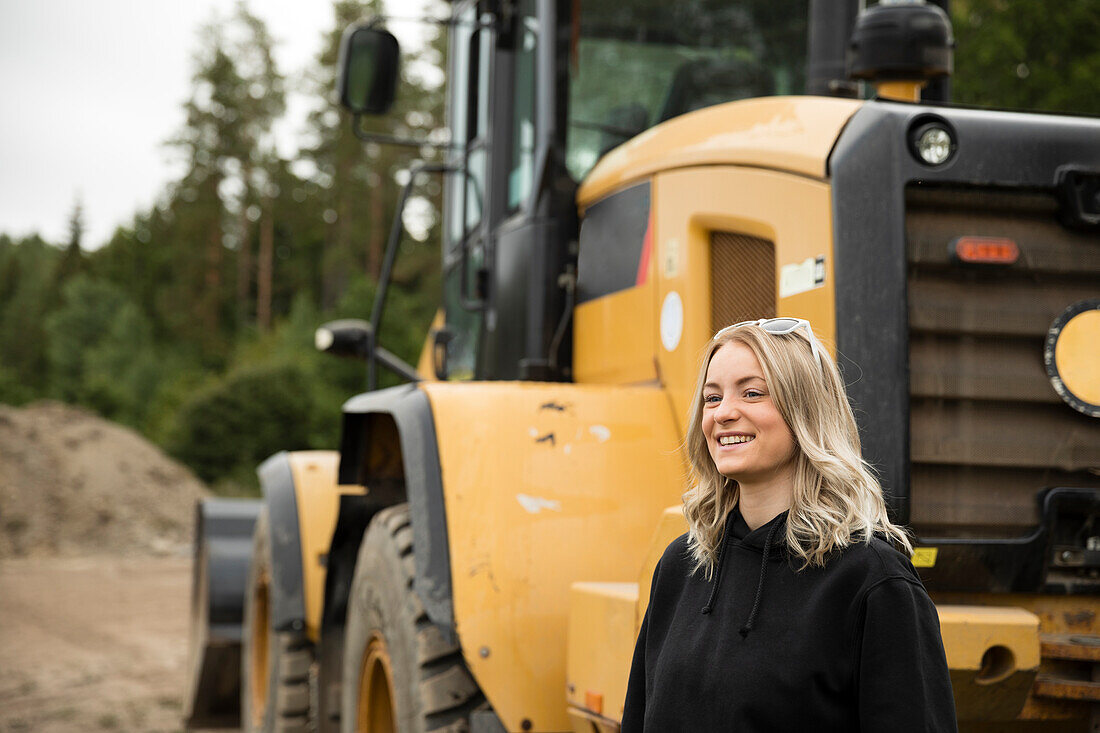 Smiling young woman standing next to excavator