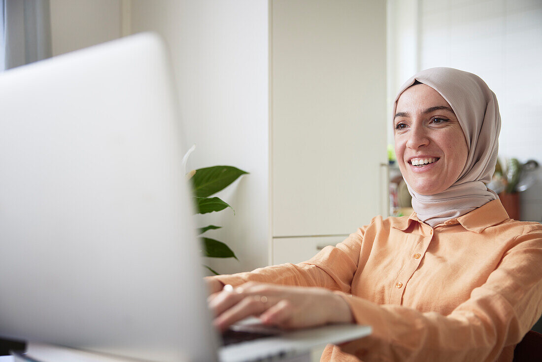 Smiling woman with hijab using laptop