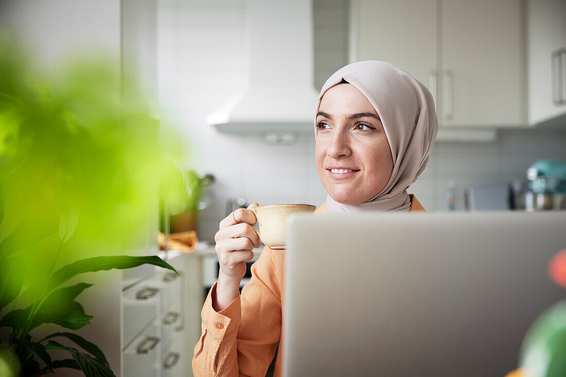 Smiling woman with hijab having coffee