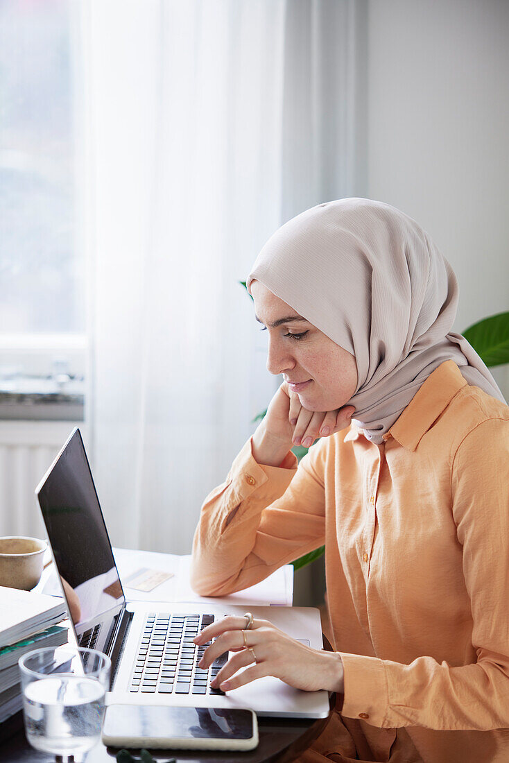 Smiling woman with hijab working from home using laptop