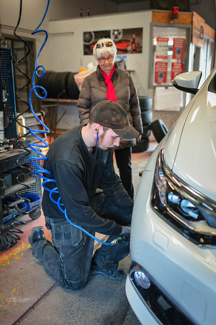 Mechanic in garage changing tires on car and talking to female client